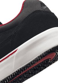 Čierne semišové a textilné tenisky s textúrovanou bielou špičkou a červeným prúžkom. Podrážka má vzorovaný grip dizajn.