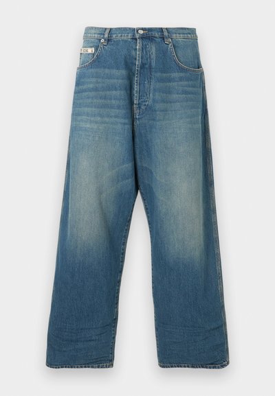 Μπλε τζιν παντελόνι με φαρδιά μπατζάκια και ξεβαμμένες περιοχές στα μπροστινά μπούτια, με πέντε τσέπες, κούμπωμα με κουμπί και θηλιές για ζώνη, παρουσιάζεται σε απλή φόντο.