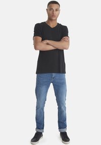 Svart v-hals t-skjorte, slim-fit lyseblå jeans og svarte joggesko. antrekket har et uformelt design med oppbrettede ermer på jeansene.