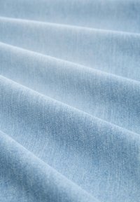 Vaaleansininen denimkangas, jossa on sileä rakenne, hienovarainen kudontakangas ja hieman ryppyisiä taitoksia.