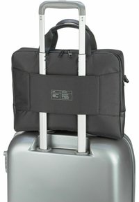 Sac à dos noir pour ordinateur portable attaché à une valise rigide argentée, avec une surface texturée, des fermetures éclair doubles et une sangle adjustable pour plus de sécurité.