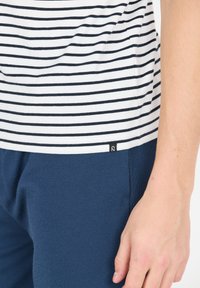 Gestreept shirt in wit en marineblauw katoen met een afgeronde zoom, gecombineerd met marineblauwe textuurbroek; voorzien van een klein logolabel nabij de zoom.