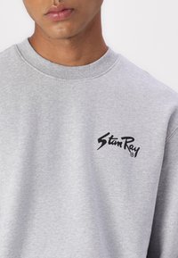 Grey sweatshirt made of cotton blend fabric, featuring a round neckline and a logo in black on the front. Smooth texture with a casual fit.