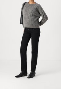 Person wearing a gray cable-knit sweater, black pants, black ankle boots, and carrying a black shoulder bag against a plain white background.