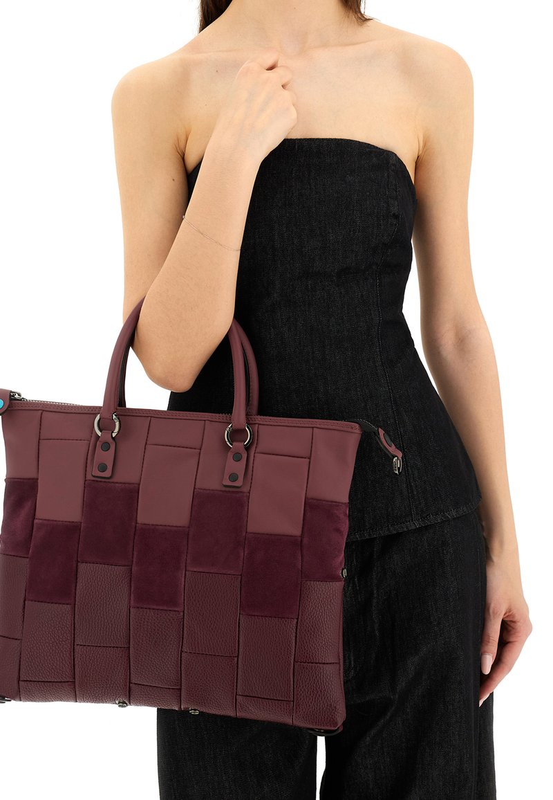 Borsa a mano bordeaux con un design intrecciato caratterizzato da texture in pelle e camoscio, manici doppi e chiusura con zip.