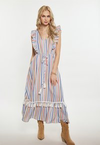 Rochie maxi cu dungi în culori pastelate, cu mâneci volanate, talie legată și accente cu ciucuri la tiv. Pur tată de cizme până la glezne de culoare bej.