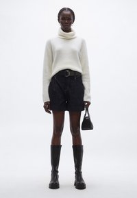 Bela pletena pulover z visokim ovratnikom, temno modri denim kratke hlače z naborki, črni škornji do kolen in majhna črna torbica. Minimalistična zasnova s čistimi linijami.