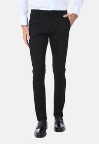 Pantaloni neri a taglio slim in tessuto testurizzato. Presentano tasche anteriori e una chiusura con bottone. Indossati con scarpe nere lucide.