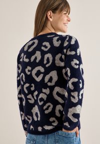 Granatowy sweter o miękkiej fakturze, z jasnoszarym wzorem w panterkę. Okrągły dekolt, długie rękawy i luźny krój, idealny na codzienne noszenie.