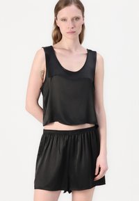 Čierny saténový crop top s okrúhlym výstrihom, v súprave s čiernymi saténovými šortkami s elastickým pásom. Hladká textúra.
