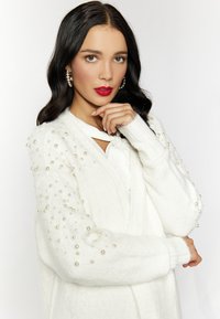 Cardigan alb realizat din material moale, cu accente din perle pe mâneci, design cu fața deschisă și o finisare texturată.