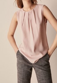 Hellrose ärmellose Bluse mit Falten detail am Ausschnitt, kombiniert mit gemusterten grauen Hosen mit maßgeschneidertem Schnitt und strukturiertem Stoff.