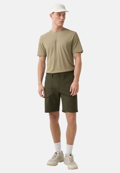 Olivgrüne Cargo-Shorts aus leichtem Stoff, mit mehreren Taschen, kombiniert mit einem beigen T-Shirt und einer weißen Kappe. Neutrale Sportsneaker.