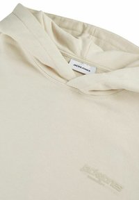 Beige hoodie made of soft fabric with a kangaroo pocket, drawstring hood, and embossed logo. Features a smooth texture and casual design.