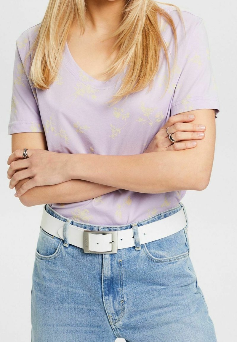 Levandulové tričko s krátkým rukávem a jemným květinovým potiskem, spárované se světle modrými džíny a bílým opaskem se stříbrnou sponou.