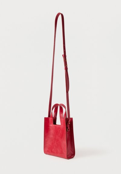 Sac fourre-tout en cuir rouge avec un design structuré, doté d'une poignée découpée carrée et d'une longue sangle ajustable. Texture lisse et quincaillerie minimaliste.