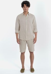 Beige linnen kortemouwen overhemd met knoopsluiting, gecombineerd met bijpassende linnen shorts. Casual fit, effen textuur, gedragen met groene espadrilles.