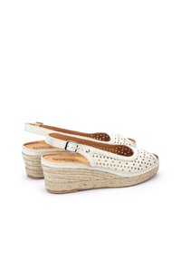 Sandalias de cuña blancas perforadas con una suela de textura yute y correa ajustable en el tobillo. Presentan punta abierta y diseño de patrón recortado.