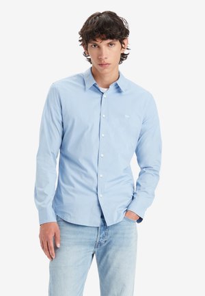 Light blue button-up shirt with a standard collar, long sleeves, and a plain texture. Includes white buttons and a small logo on the chest.