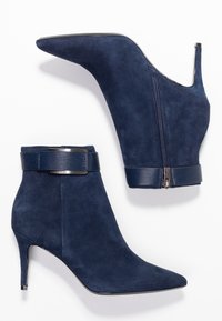 Navyblauwe suede enkellaarsjes met een spitse neus, stilettohak en een gestructureerde enkelband met een gepolijste metalen accent. Zijkant ritssluiting.