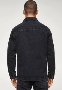 Chaqueta vaquera negra con corte recto, cierre frontal con botones y cuello puntiagudo. Presenta doble costura y bolsillos laterales. Se muestra la vista trasera.