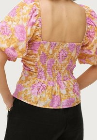 Blumenbluse mit Puffärmeln, mit gerafftem Rücken in rosa und gelben Farbtönen, mit quadratischem Ausschnitt und strukturiertem Stoff.