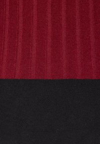 Tissu tricoté présentant une texture côtelée rouge sur la moitié supérieure et une moitié inférieure noire unie, créant un design bicolore distinct.