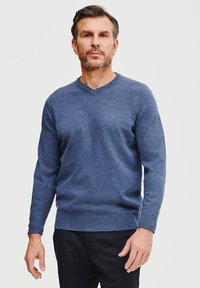 Niebieski sweter dzianinowy w fasonie v-neck, z prążkowanymi mankietami i dołem. Miękka faktura i dopasowany krój, w połączeniu z ciemnymi spodniami.
