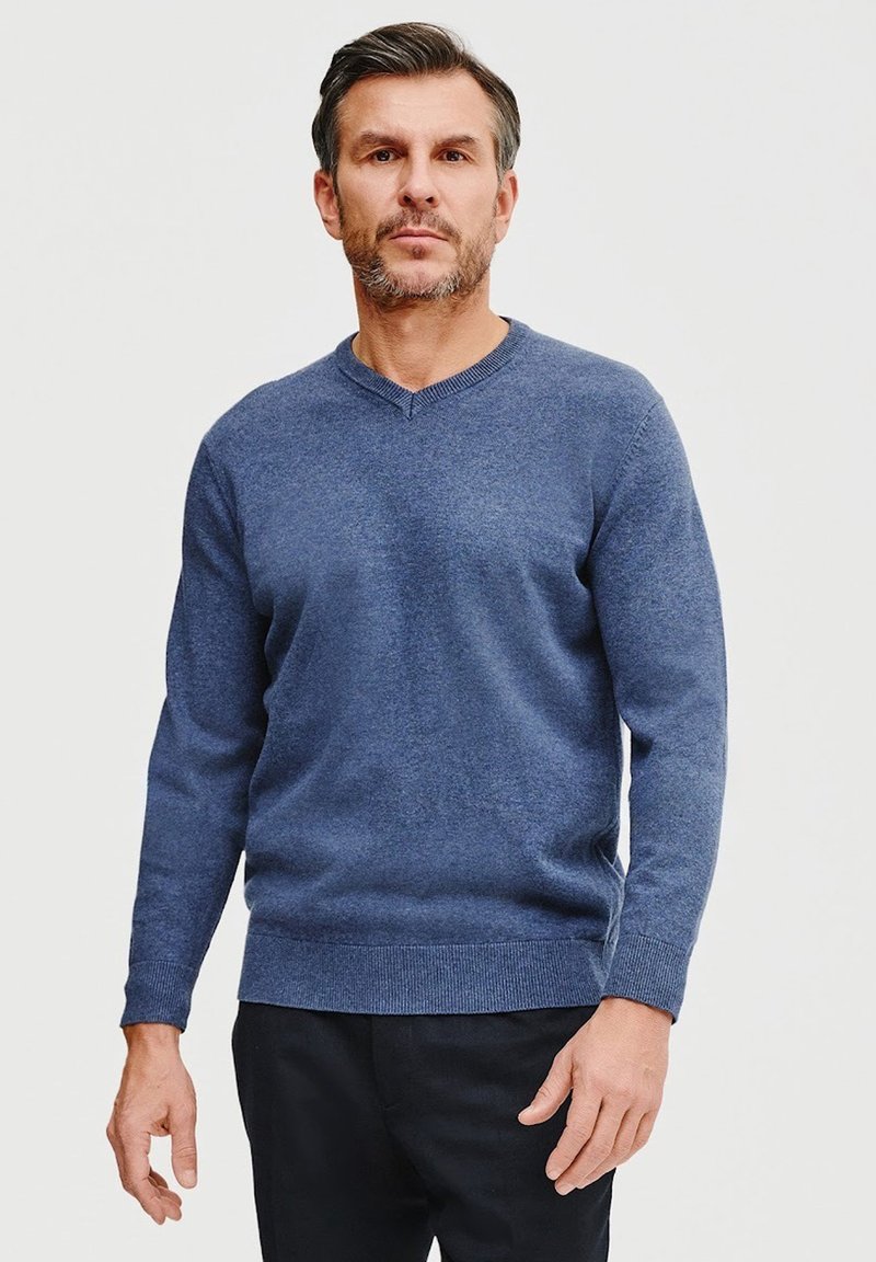 Niebieski sweter dzianinowy w fasonie v-neck, z prążkowanymi mankietami i dołem. Miękka faktura i dopasowany krój, w połączeniu z ciemnymi spodniami.