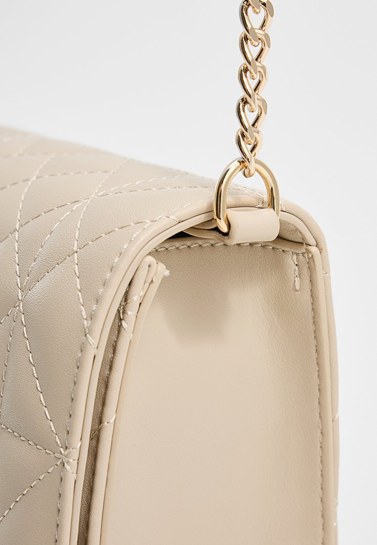 Bolso de mano de cuero acolchado beige con correa de cadena dorada, mostrando un primer plano de la esquina superior y los detalles de costura. Textura suave.
