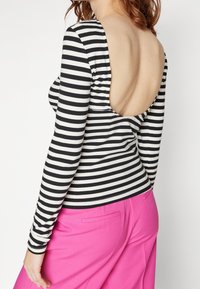 Långärmad tröja med svart och vita horisontella ränder, med en djup utskärning i ryggen. Kombinerad med högmidjade rosa byxor.