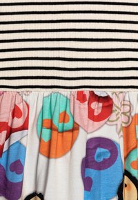 Gestreepte geribde bodice in zwart en crème overgaat in een geplooide onderkant met kleurrijke hartpatronen op een lichte achtergrond.