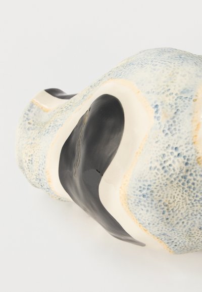 Γυαλισμένο κεραμικό γλυπτό με υφή μπλε-γκρι επιφάνειας και ομαλές καμπυλωτές μαύρες και λευκές ενότητες, απεικονίζεται σε λευκό φόντο.