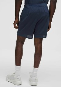 Granatowe szorty sportowe z siateczkowej tkaniny, z elastycznym paskiem ze sznurkiem i kieszeniami po bokach. W komplecie z białymi butami sportowymi i skarpetkami.