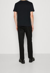 Maglietta nera a maniche corte e pantaloni neri, entrambi in tessuto liscio. Design semplice con una vestibilità rilassata, abbinati a scarpe nere.