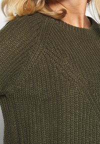 Olivgrüner, gestrickter Pullover mit strukturiertem Rippenmuster, rundem Ausschnitt und enganliegender Silhouette.