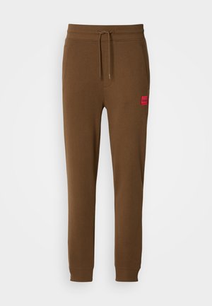 Brown jogger pants with elastic waistband and drawstring, ribbed cuffs, side pockets, and small red "HUGO" logo patch on left thigh.