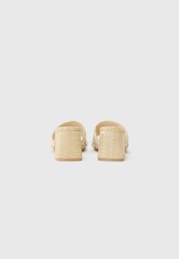 Beige vevde mules med en teksturert finish, som har en bred stropp og en chunky, lav hæl. Enkel, ren design med et naturlig utseende.