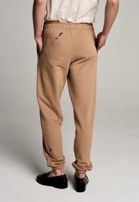 Braune Jogginghose mit elastischem Bund, einer einzelnen Gesäßtasche mit blauen Farbspritzern, schmal zulaufenden Bündchen und weichem Baumwollmischgewebe.
