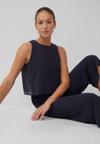 Marineblauw mouwloos topje met een losse pasvorm en doorschijnende overlay, gecombineerd met bijpassende brede broek. Soepele stof, minimalistisch ontwerp.