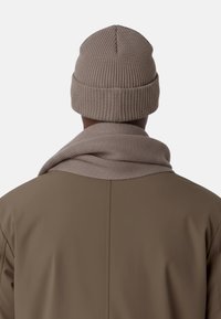 Bonnet en tricot marron à texture côtelée, assorti à une écharpe portée sur une veste marron, vu de dos.