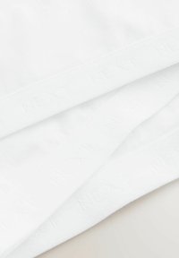 Biała bawełniana tkanina o gładkiej fakturze, z paskiem z napisem "NEXT" powtórzonym w wytłaczanym druku wzdłuż krawędzi.