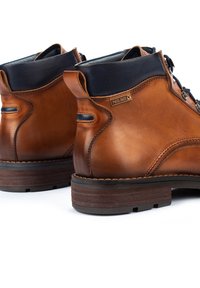 Bottes chevilles en cuir marron avec un col bleu marine, à lacets à l'avant et finition texturée. Comprend une étiquette de marque et une semelle en cuir marron robuste.