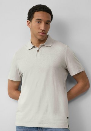 Hellbeige Poloshirt mit kurzen Ärmeln, weicher Textur, klassischem Kragen und Zwei-Knopf-Leiste; der Saum hat ein kleines Markentäschchen.