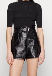 Top noir à côtes avec un col haut et des manches courtes, associé à un short en simili cuir noir taille haute avec une finition brillante et une ceinture.