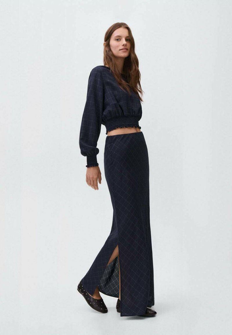 Námornícky károvaný dvojdielny outfit so skrátenou blúzkou s volánovými rukávmi a dlhou sukňou s bočnými rozparkami. Ploché topánky so študentskými detailami.