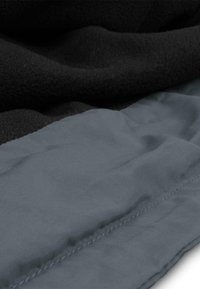 Schwarzes Fleece und grauer Nylonstoff sind übereinander geschichtet, mit sichtbaren Nähten im grauen Bereich, was ein strukturiertes Erscheinungsbild erzeugt.