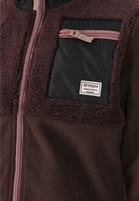 Maroon fleece jacket with a contrasting black pocket, featuring a zipper. Textured fabric and a tag marked "ZIGZAG ACTIVE LIFESTYLE" present.
