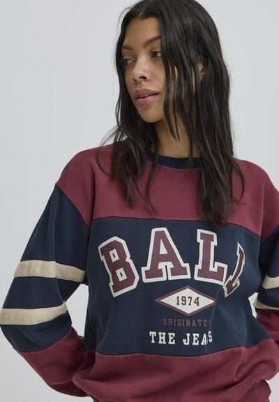 Bordo ja tumesinine värvikombinatsiooniga dressipluus kreemjast triibuga. Üksikasjadena on esiplaanil julge "BALL" logo, aastaarv 1974 ja tekst "ORIGINATED THE JEANS". Valmistatud puuvillast.