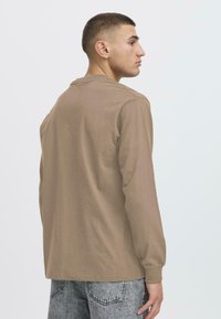 Langarmhemd aus khakifarbenem Baumwollstoff, mit Rundhalsausschnitt und lockerem Schnitt. Die Textur wirkt weich; minimalistisches Design ohne sichtbare Muster.